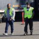 Four men wearing safety vests and work clothing walk together across a trucking yard with trailers behind them.