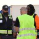 Three people wearing reflective safety vests stand together in a trucking yard during a training or safety discussion.