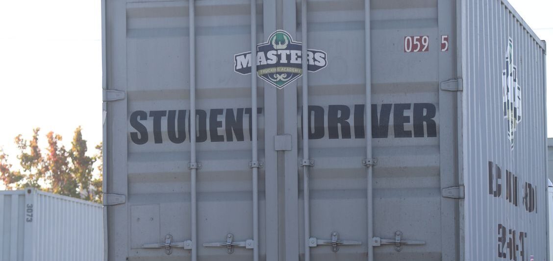 Rear view of a training trailer marked “Student Driver” parked in a commercial trucking yard.
