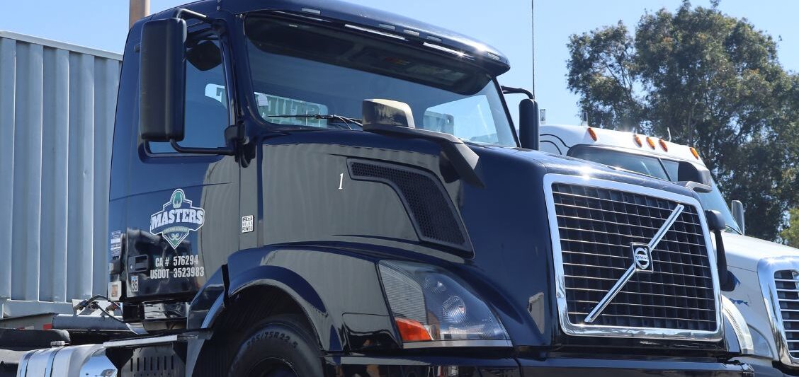 Black semi-truck cab parked in a lot beside a white trailer and another truck on a clear day.