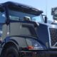 Black semi-truck cab parked in a lot beside a white trailer and another truck on a clear day.
