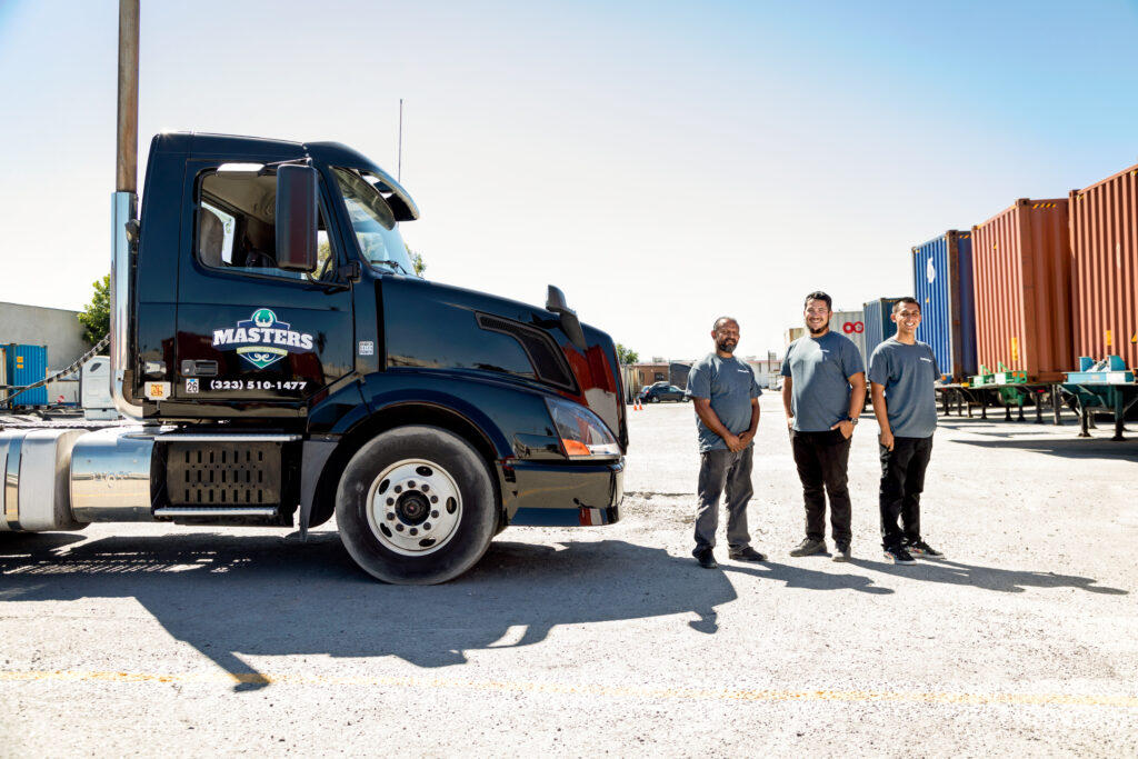 Semi-truck parked at a trucking facility with several people standing nearby.