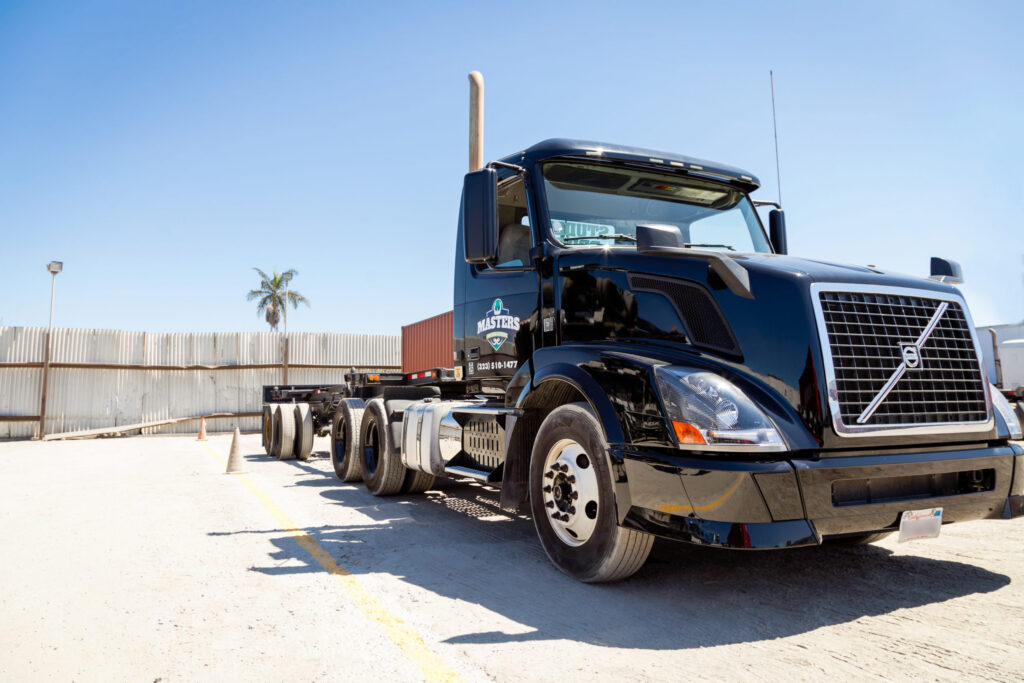 Blue semi-truck with a flatbed trailer parked at a commercial trucking facility.