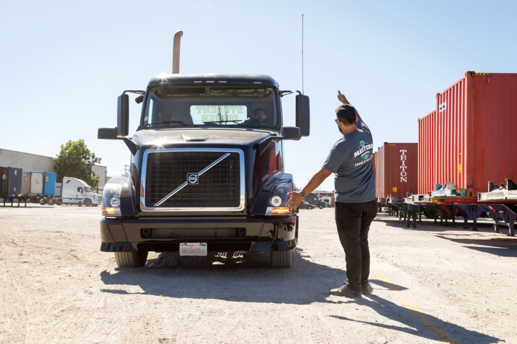 Semi-truck parked near shipping containers with a person standing beside it.