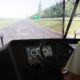 A man wearing a high-visibility vest sits at the controls of a truck driving simulator displaying a highway scene.